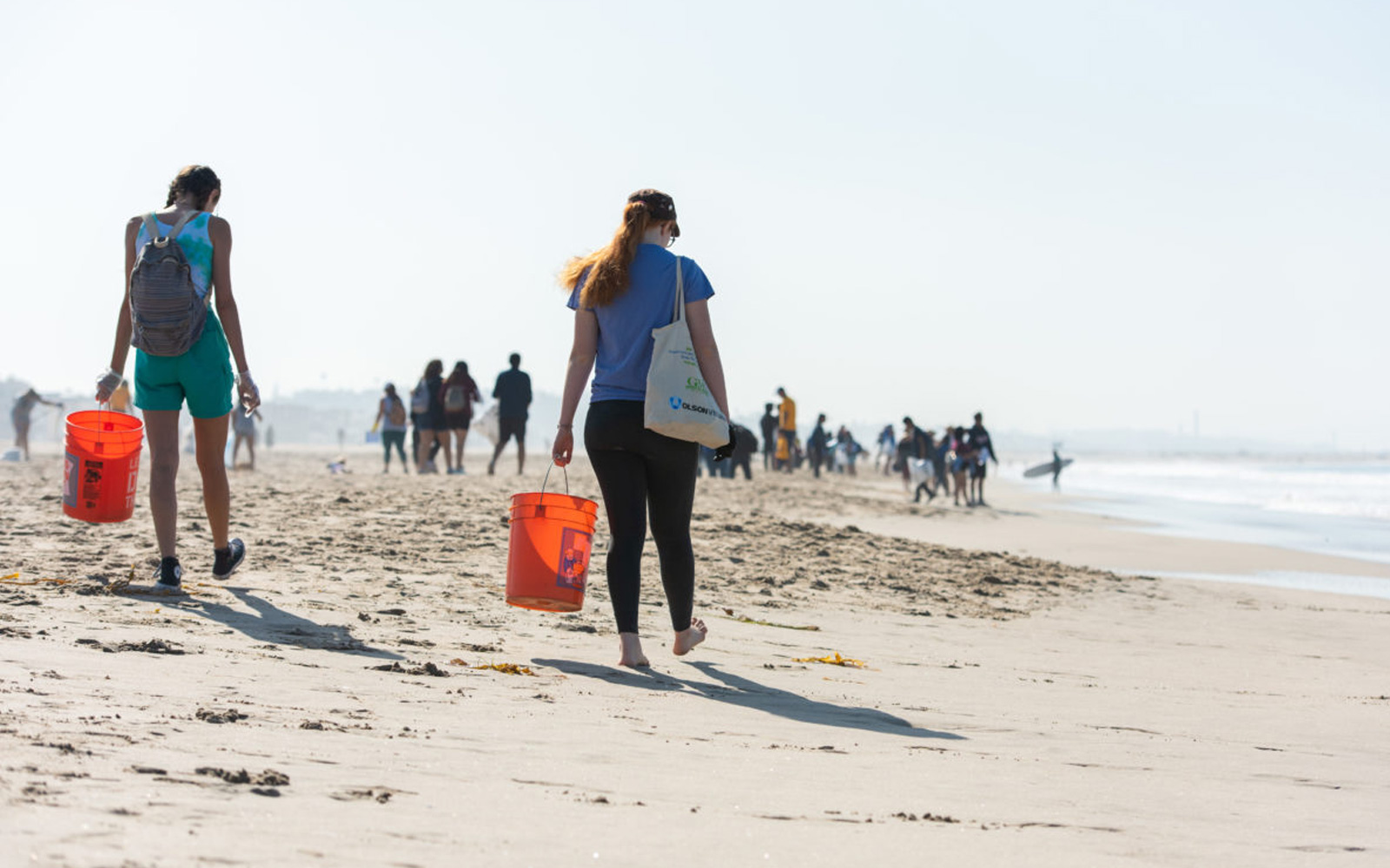 Volunteers carrying orange buckets while cleaning up a beach, highlighting community actions promoted in the LA County water FAQ to protect coastal water quality.