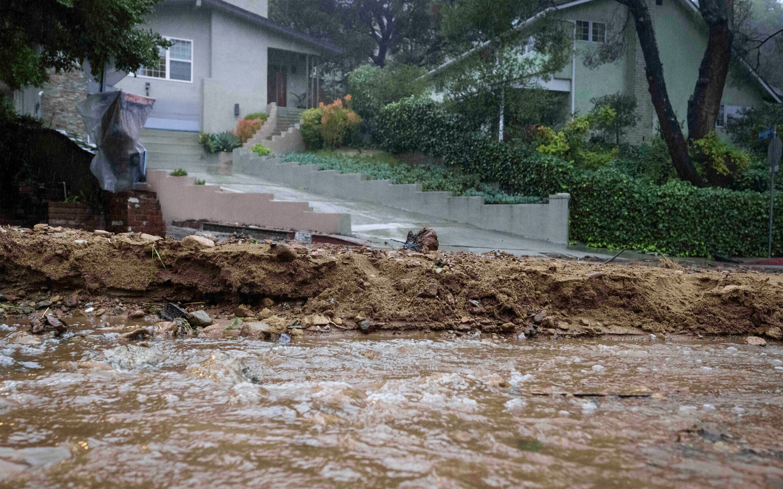 A view of a heavily flooded residential street with rushing brown water, demonstrating the high-risk areas detailed in the LA County water FAQ.