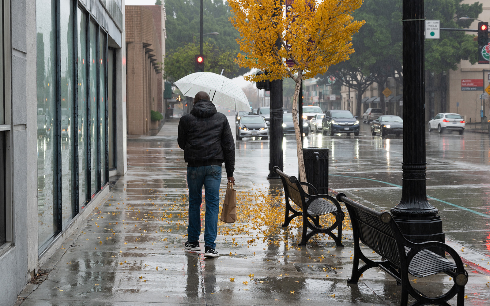 A person holding a white umbrella walking down a rain-slicked city sidewalk, reflecting the urban storm readiness tips found in the LA County water FAQ.