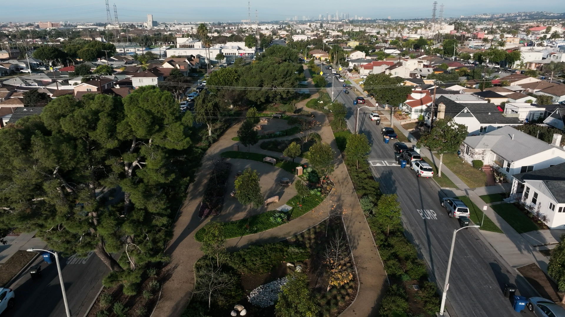 An aerial view of a wide residential street in East Los Angeles featuring landscaped sustainable medians with drought-tolerant plants and walking paths.