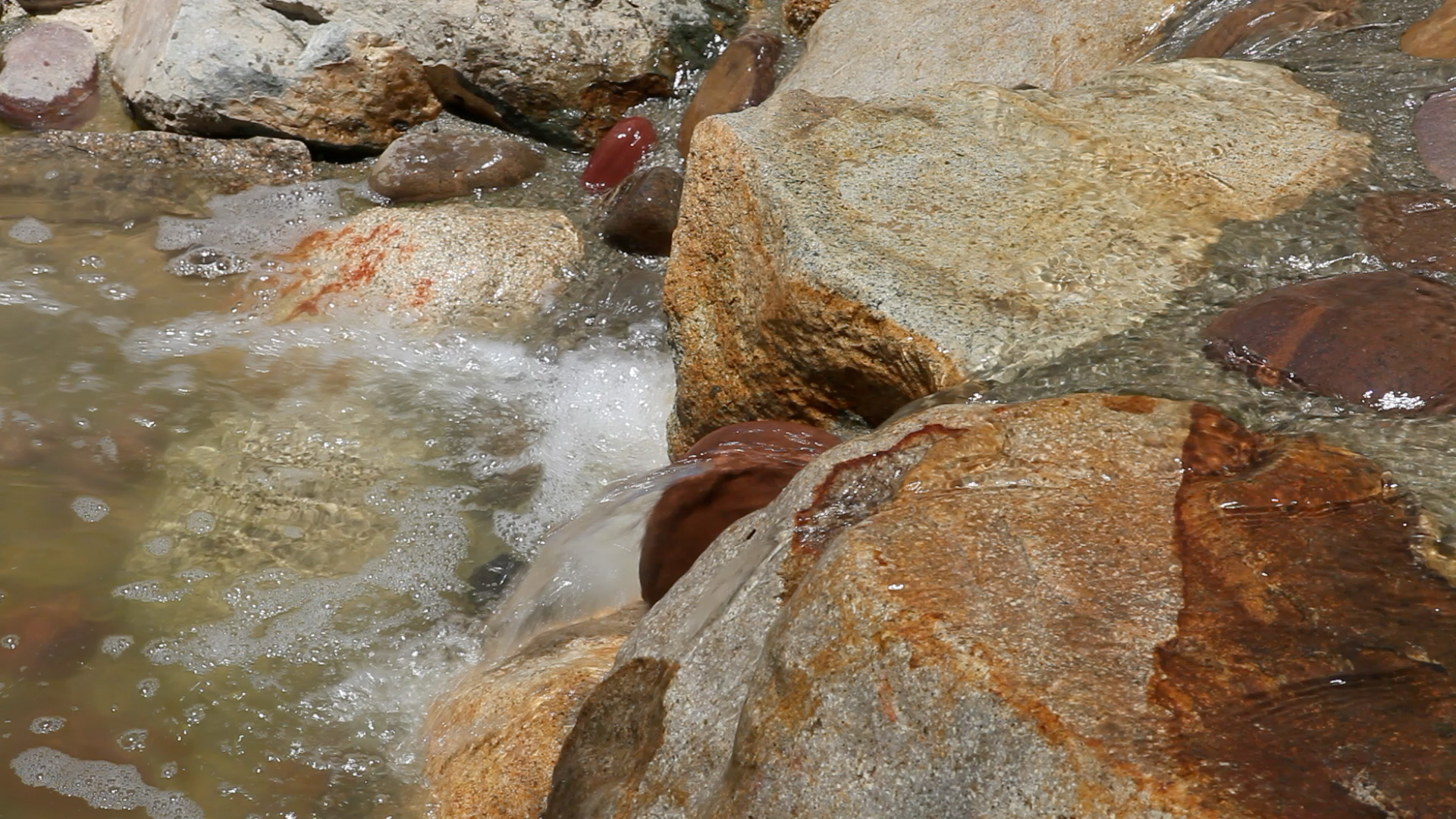 A close-up view of clear water flowing quickly over smooth, light-colored river rocks and pebbles
