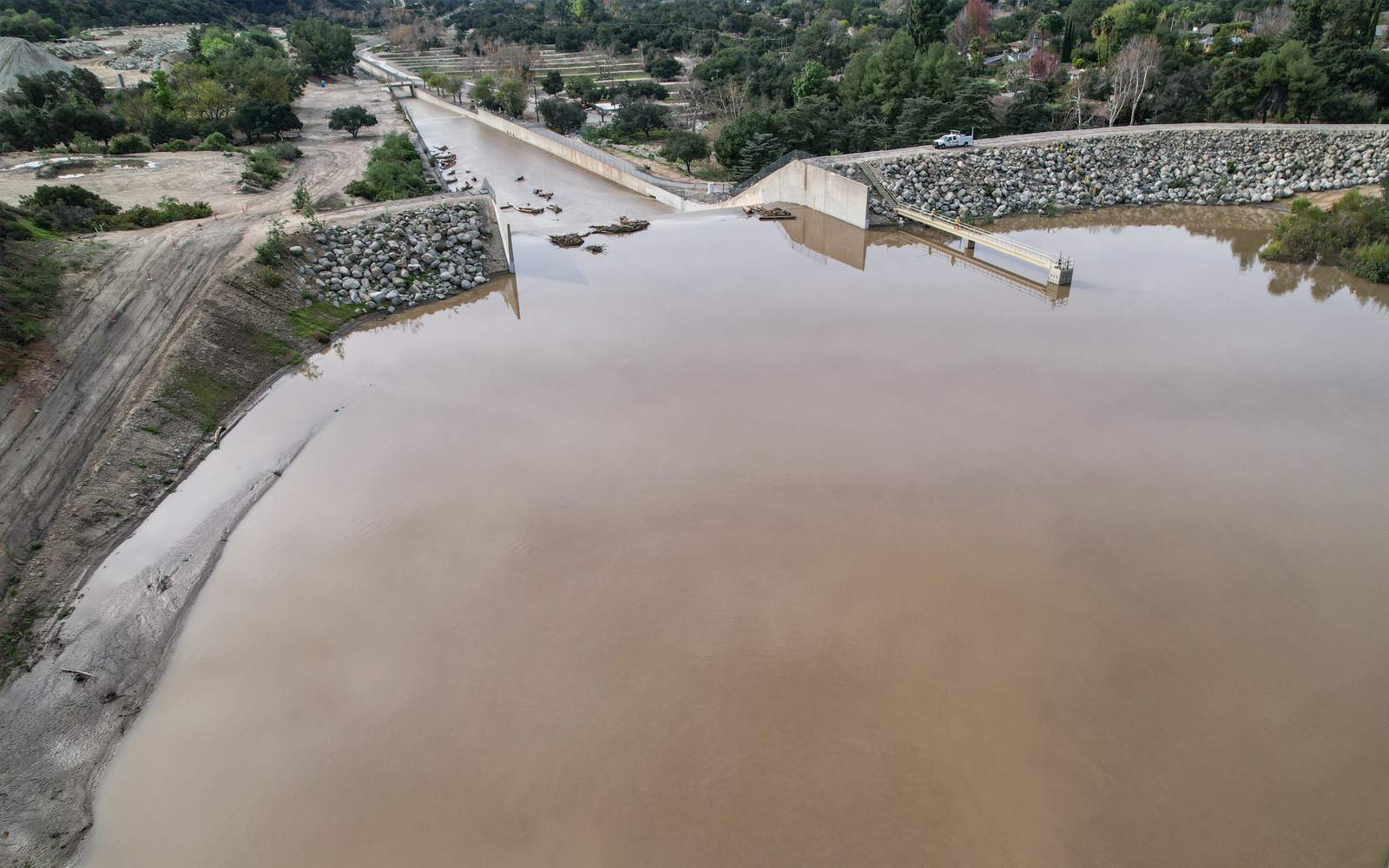 Aerial view of a large concrete debris basin filled with brown stormwater runoff in a mountainous region