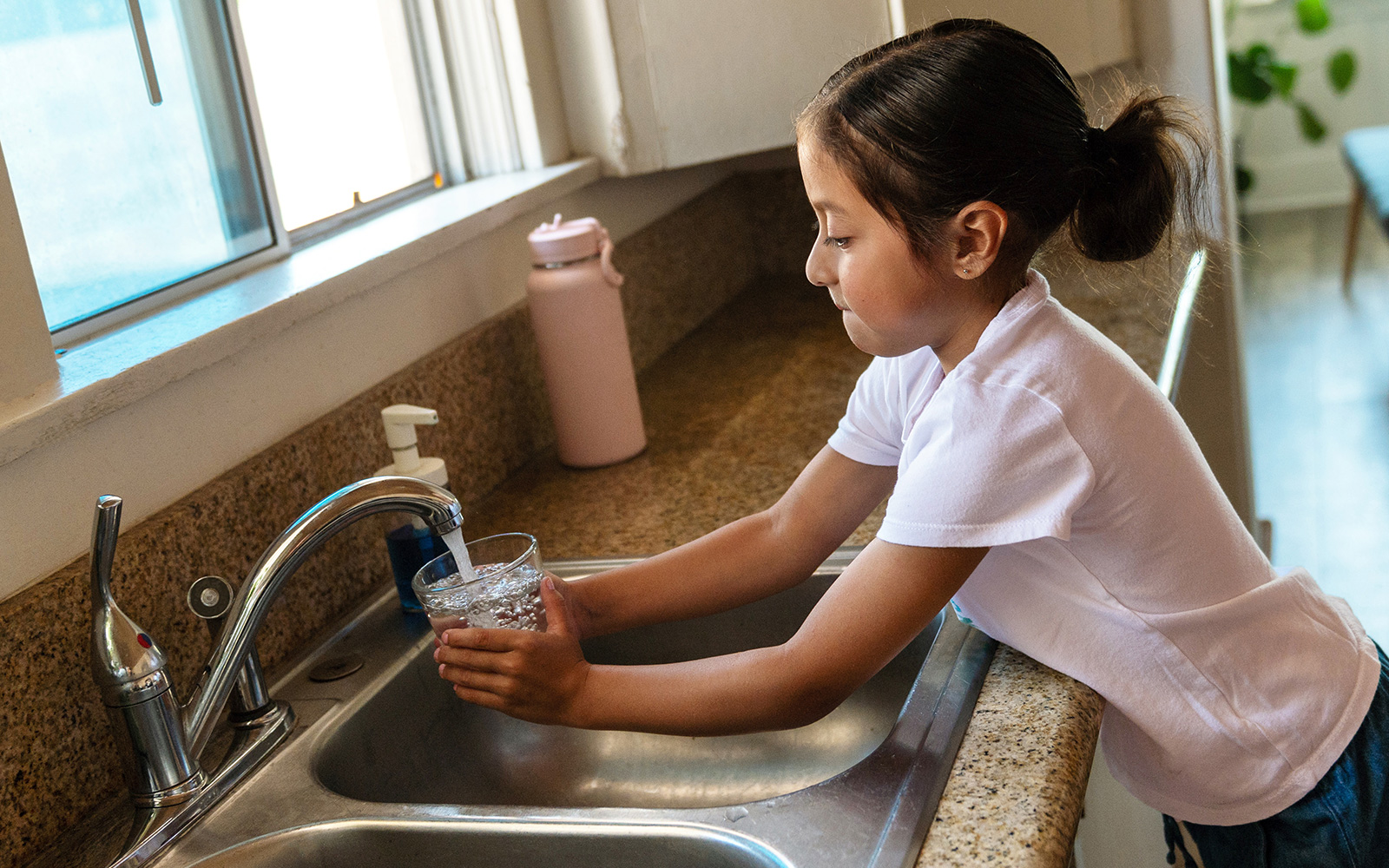 A child pouring a glass of water from a kitchen faucet