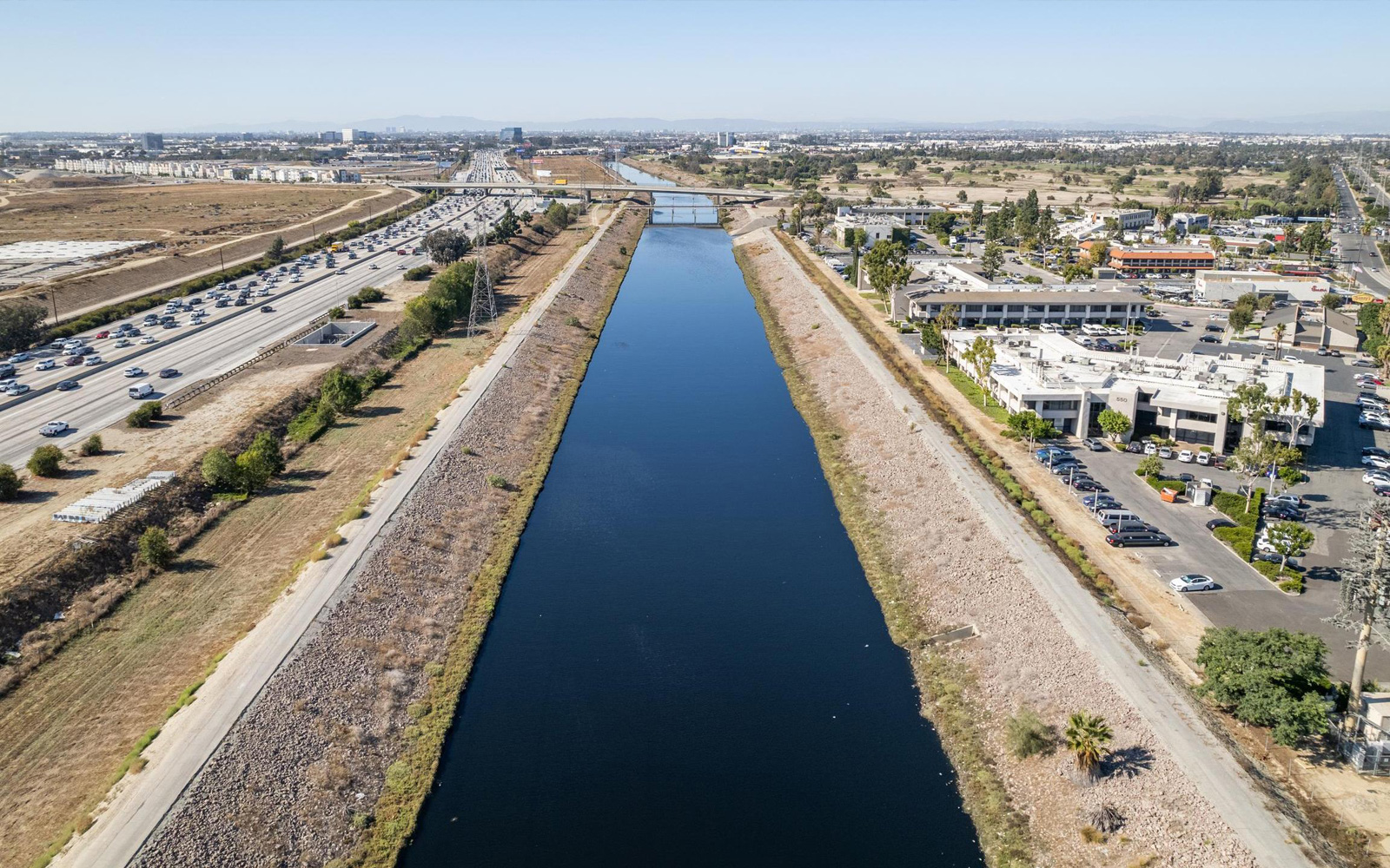 Aerial view of a concrete flood control channel filled with dark blue water running through an urban neighborhood