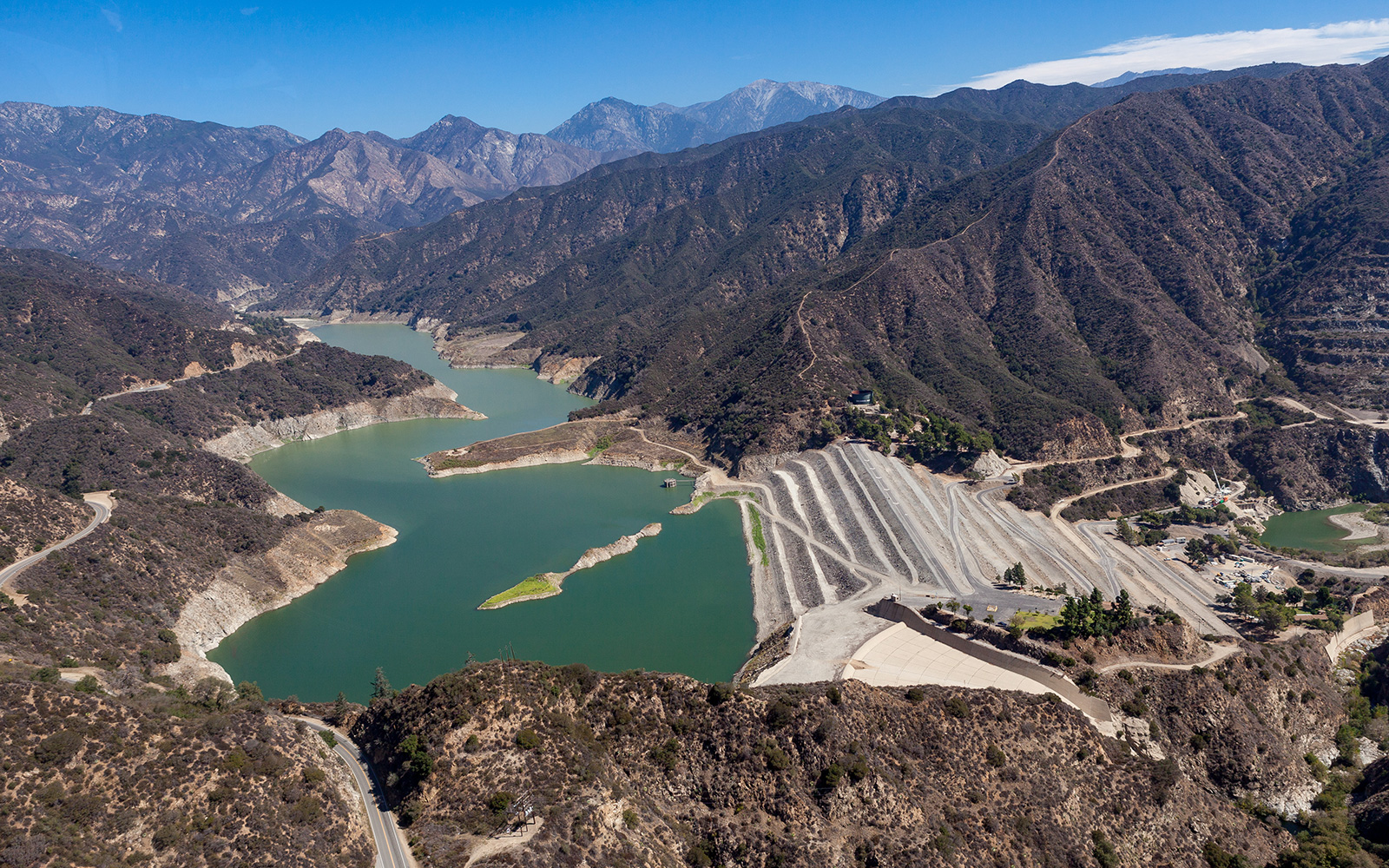 An aerial photo of the San Gabriel Dam featuring the reservoir and the surrounding rugged mountain terrain