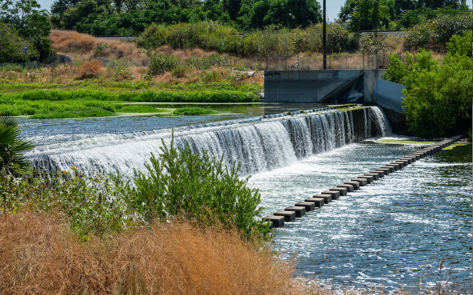 A wide view of a concrete spillway at a spreading ground facility with water cascading over the edge
