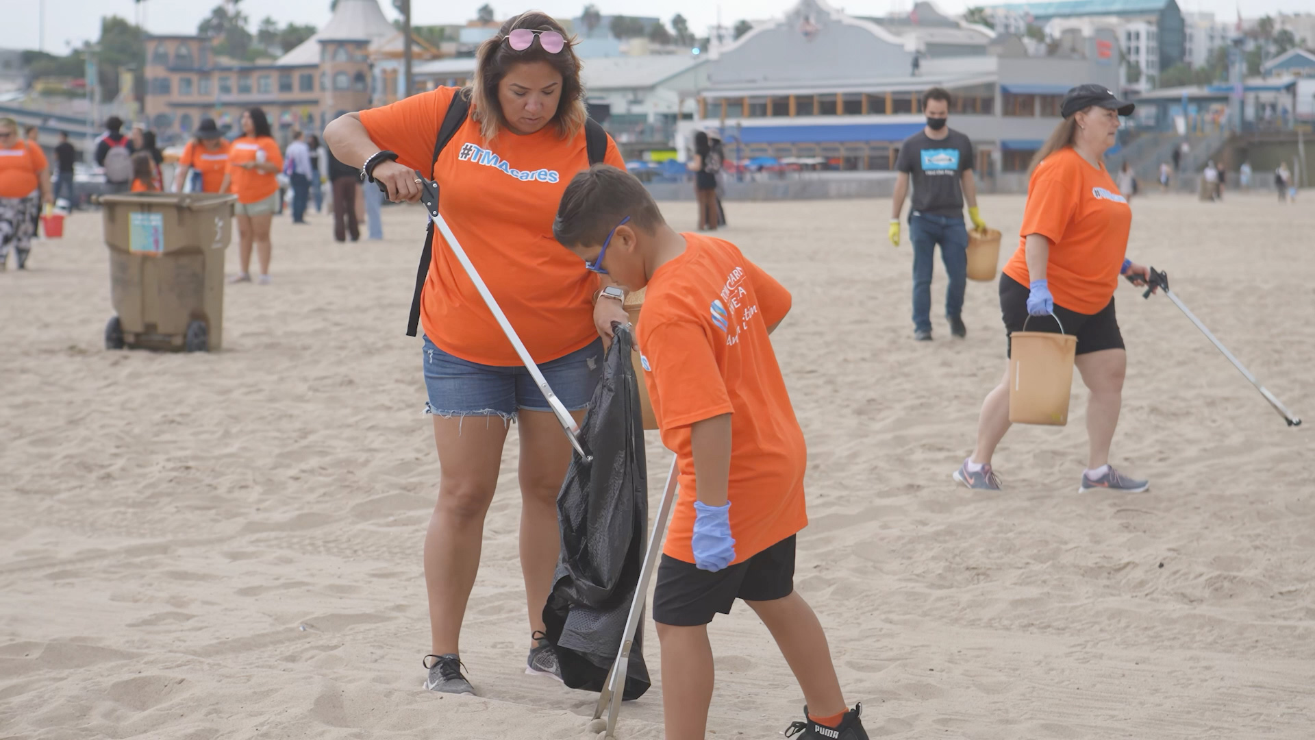A group of volunteers in orange shirts collecting trash on a sandy beach during a community cleanup event